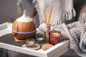 Aroma diffuser, candles, and reed sticks on a tray next to a cozy knit blanket — a comforting gift idea for a loved one in a long-term care facility.