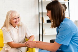 A nurse holds hands with an elderly woman, both smiling warmly.