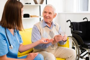 A nurse gives medication to an elderly man in a cozy room.