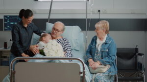 A family visits an elderly patient in the hospital, bringing flowers and sharing a hug.